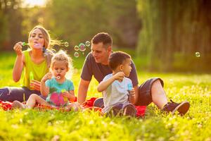 Familie sitzt im Park auf einer Decke und pustet Seifenblasen