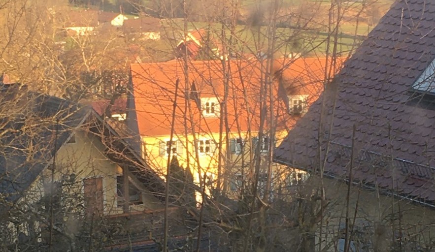 Bild vergrößern: Auf dem Bild sind zwei Häuser und eine Scheune zu sehen. Zwischen den beiden Häusern steht ein gelber Scheune mit weißen Fenstern und blauen Fensterläden. Der Scheune hat 3 Stockwerke.