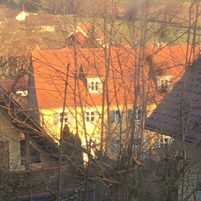 Auf dem Bild sind zwei Häuser und eine Scheune zu sehen. Zwischen den beiden Häusern steht ein gelber Scheune mit weißen Fenstern und blauen Fensterläden. Der Scheune hat 3 Stockwerke. 