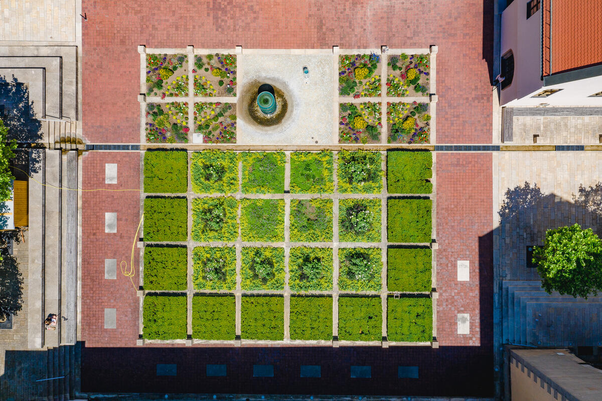 Bild vergrößern: Luftbild des Münter Platzes. Ein in zwei und dreißig verschiedene kleine Beete mit Blumen geteilter Garten, in dessen Mitte sich eine gläserne Brunnenanlage befindet.