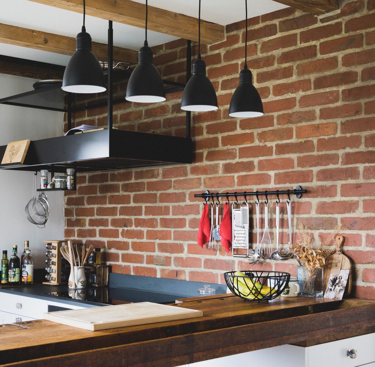 Bild vergrößern: Küche mit Ziegelwand. An der Wand hängt eine schwarze Dunstabzugshaube. Die Küchenzeile ist aus Altholz.