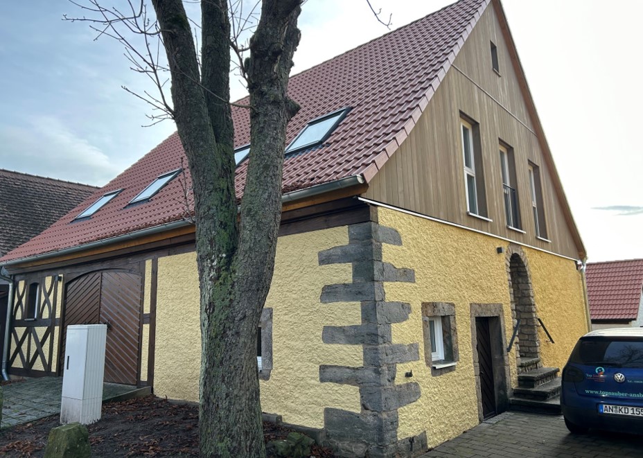 Bild vergrößern: Gelbes Haus mit einem holzverkleideten Stockwerk. An der Seite des Hauses befinden sich einige Steine in der Fassade.