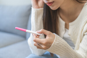 Traurige, enttäuschte junge Frau hält einen Schwangerschaftstest in der Hand.